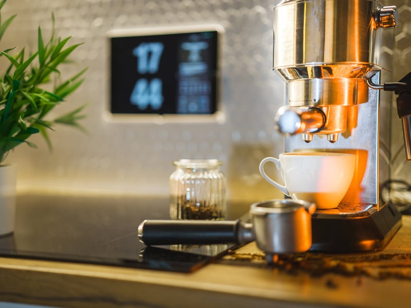 a coffee maker is sitting on a counter next to a cup of coffee with home automation controls in the background